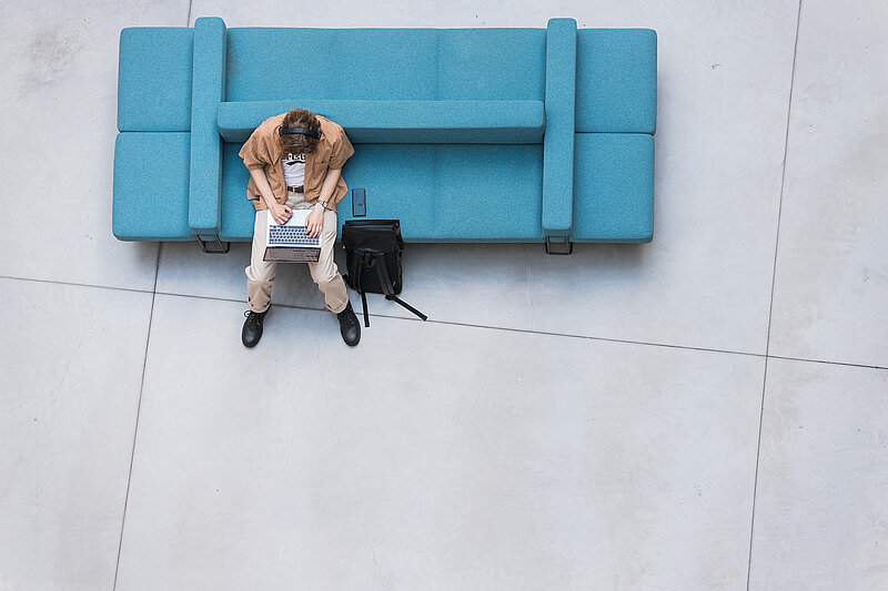 Students ar klēpjdatoru strādā LU telpās, sēžot uz zila dīvāna