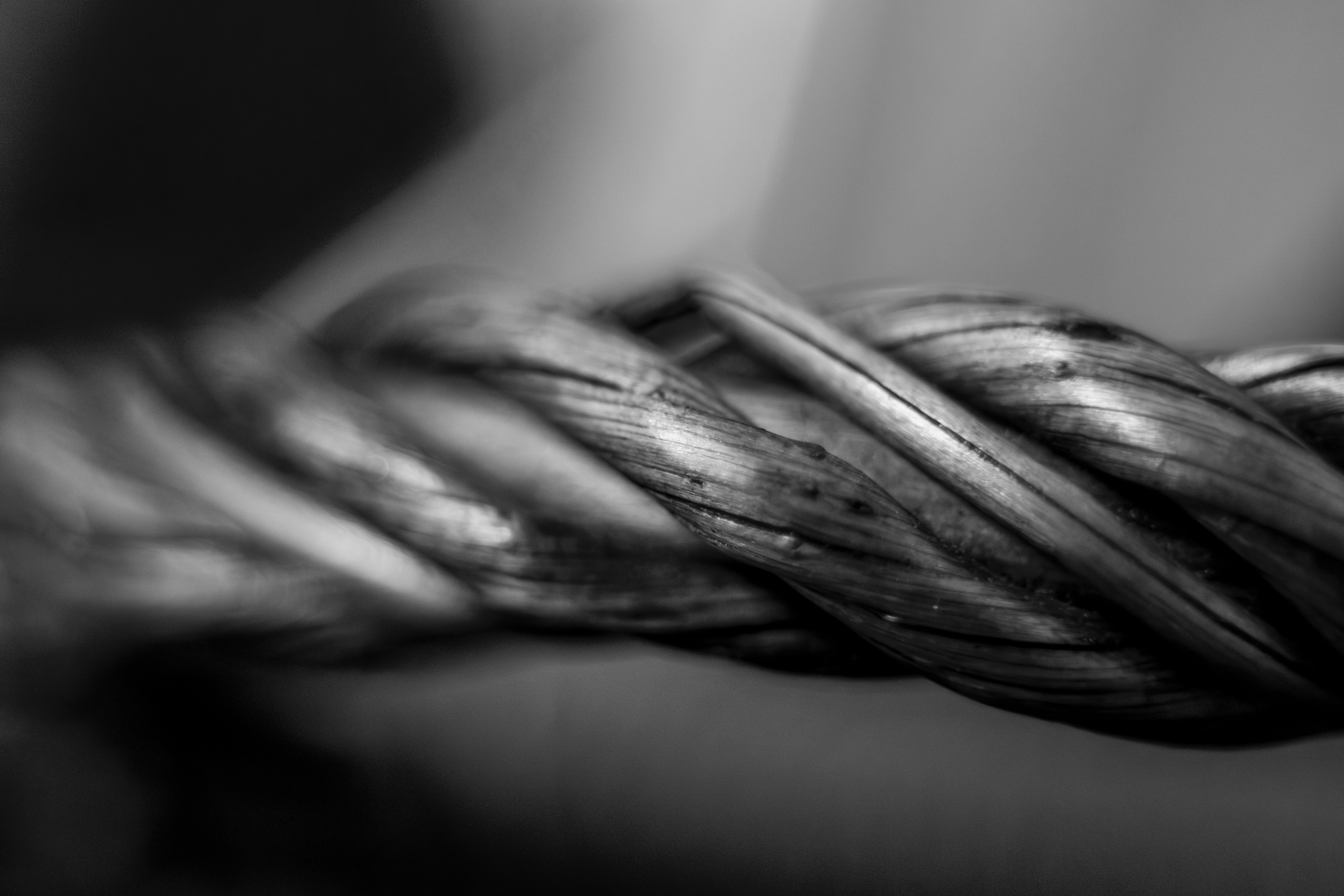 Melna un balta makro fotografija ar savītu tērauda trosi vai kabeli, kas parāda detalizētu šķiedru struktūru